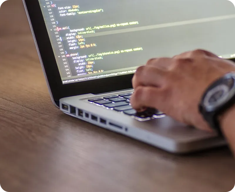 Close-up of a person typing code on a laptop keyboard with CSS code visible on the screen.