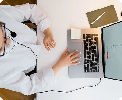 Two people, a woman and a man, focused on a laptop screen while working together at a glass table indoors.