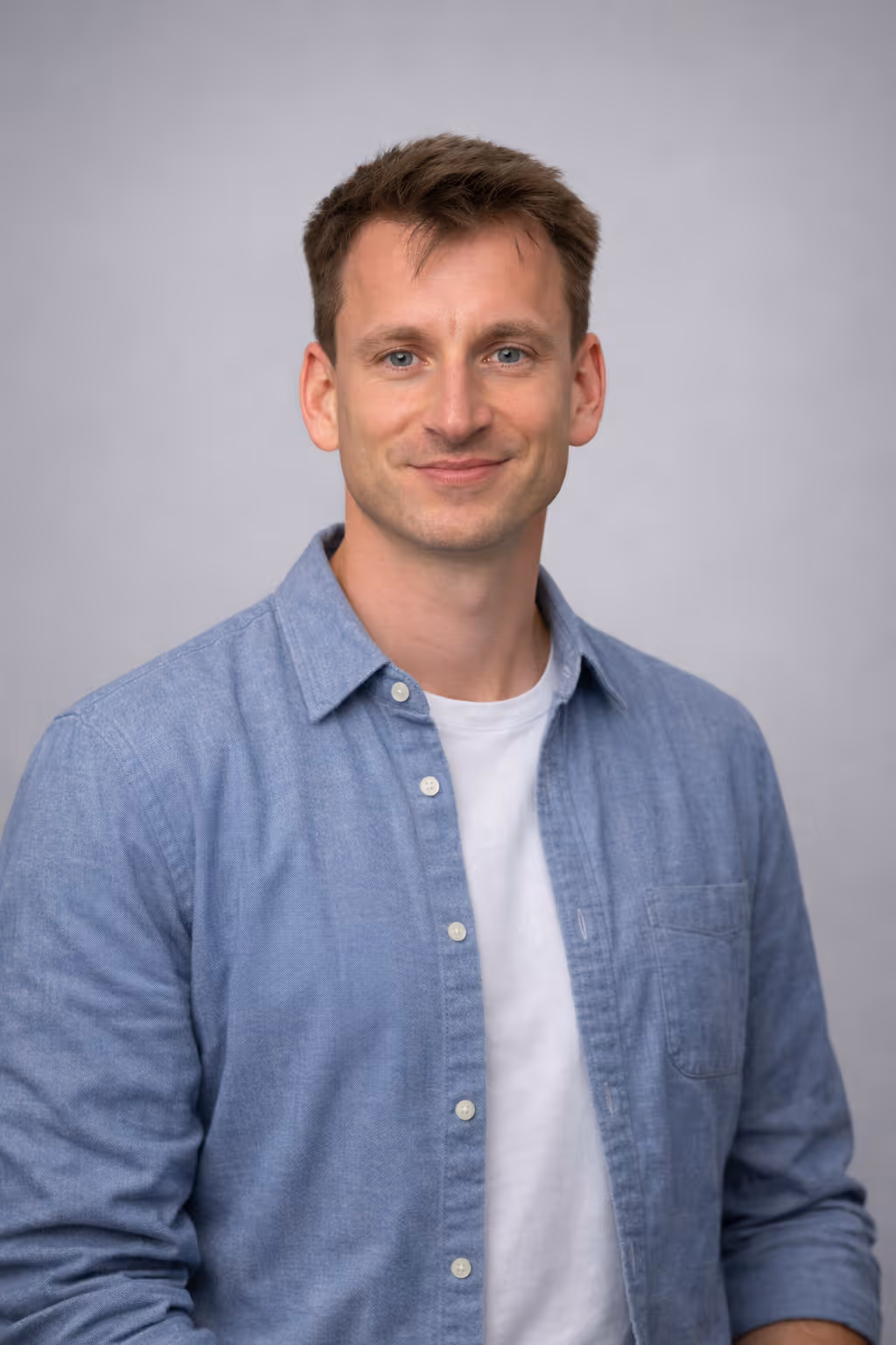 Portret van een lachende man met blauw overhemd en wit t-shirt tegen een grijze achtergrond; foto van Stijn