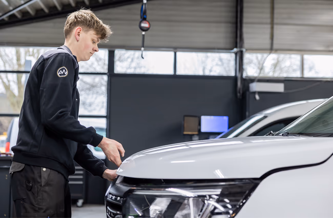 Een automonteur sluit de motorkap van een witte gecontroleerde occasion