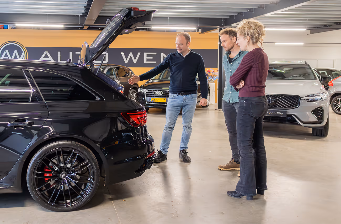 De verkoper demonstreert een leaseauto aan een echtpaar in de showroom