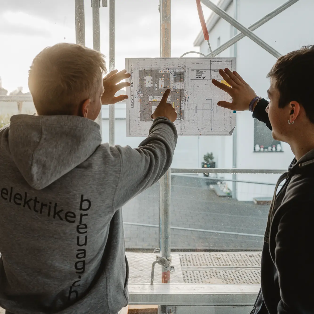 Zwei Elektriker der Breu AG besprechen am Baugerüst einen Grundriss/Elektroplan für die Installation.