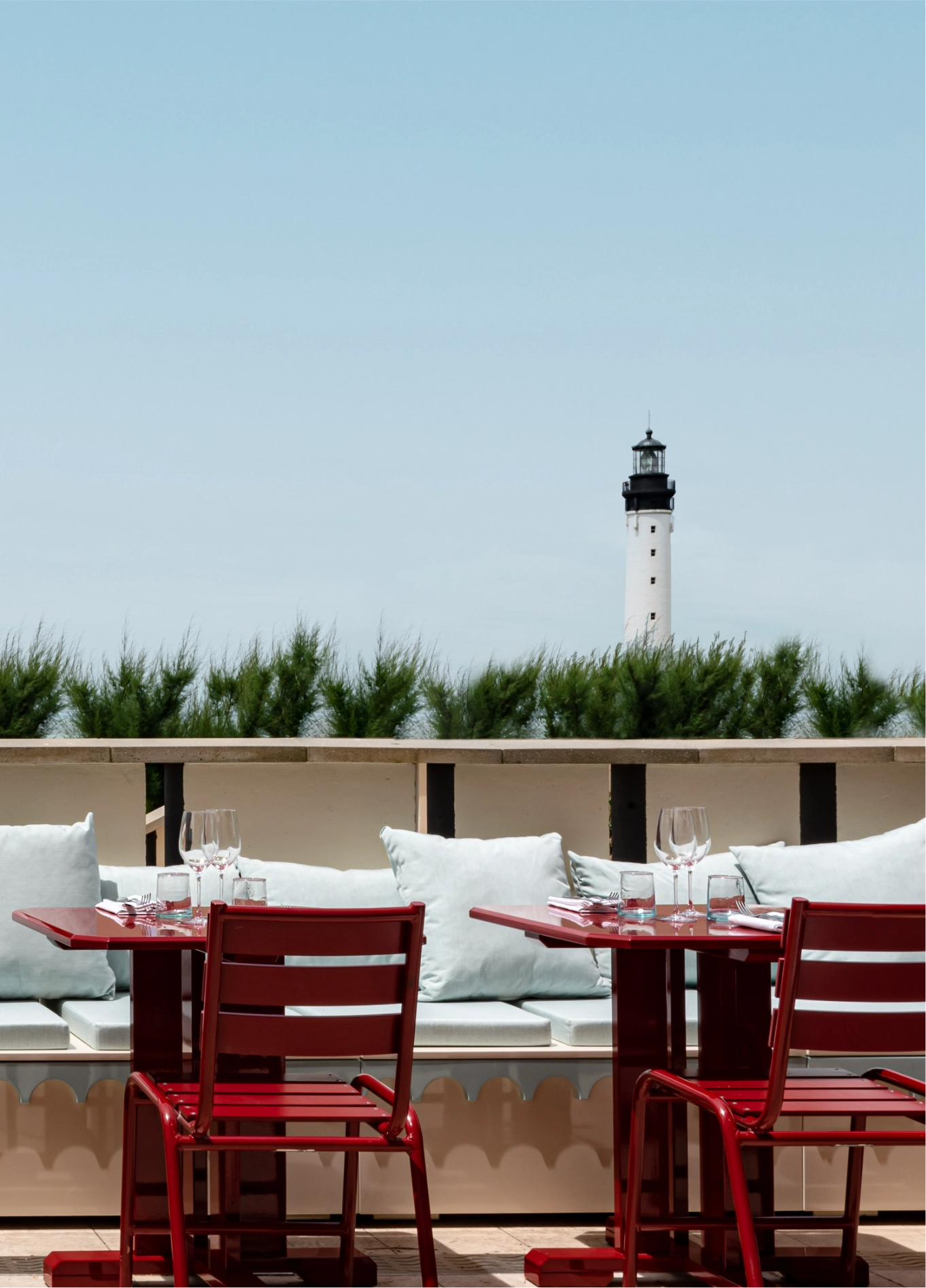 Outdoor terrace at Regina Experimental with red tables and chairs, offering a clear view towards a lighthouse in the distance.