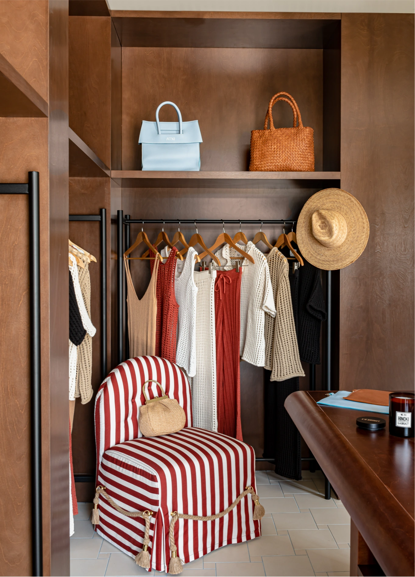 Elegant walk-in closet with hanging clothes, handbags on the top shelf, and a red and white striped armchair, creating a sophisticated atmosphere.