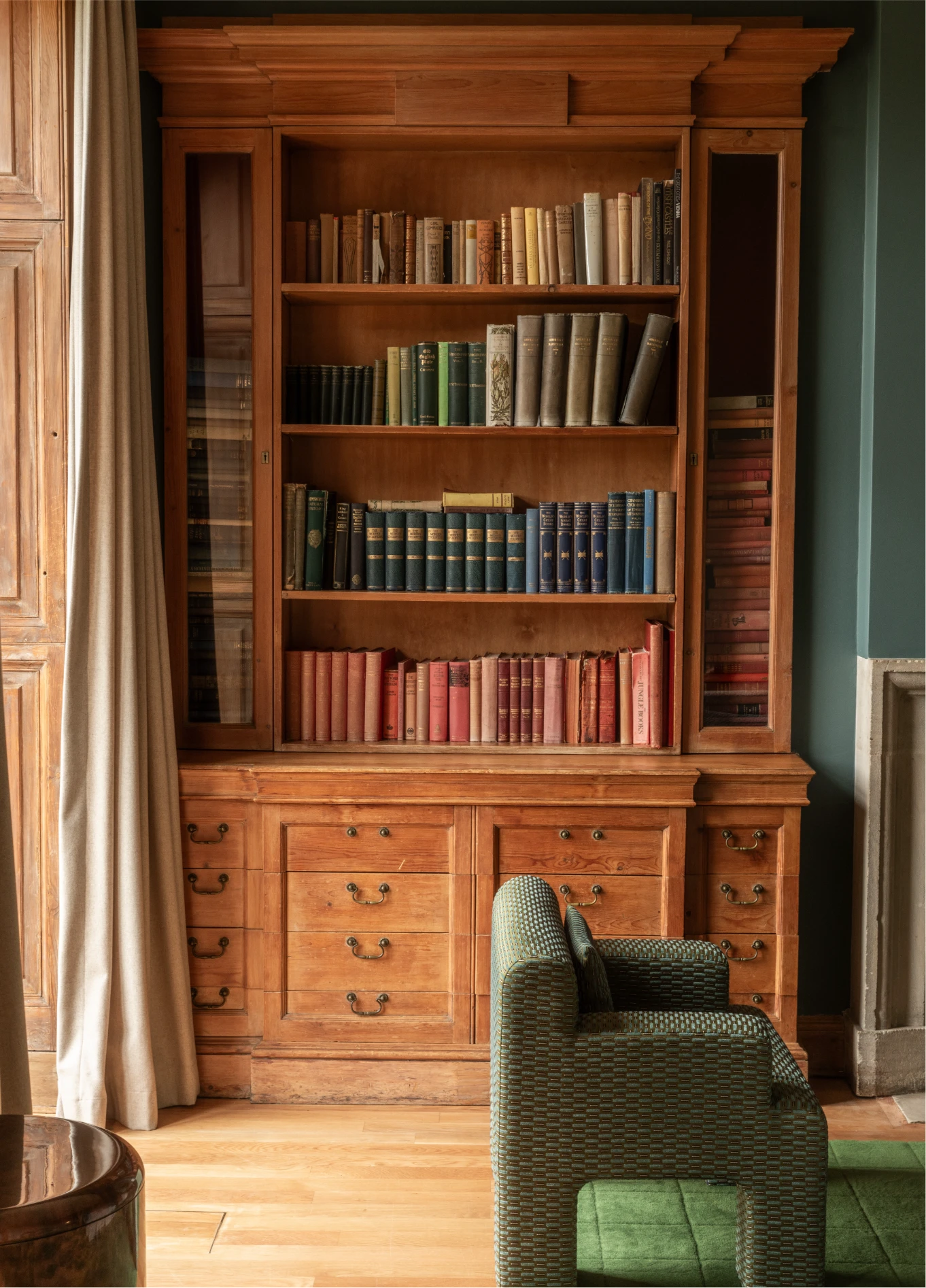 Bibliothèque en bois avec fauteuil vert dans une pièce cosy au Cowley Manor Experimental, Cotswolds