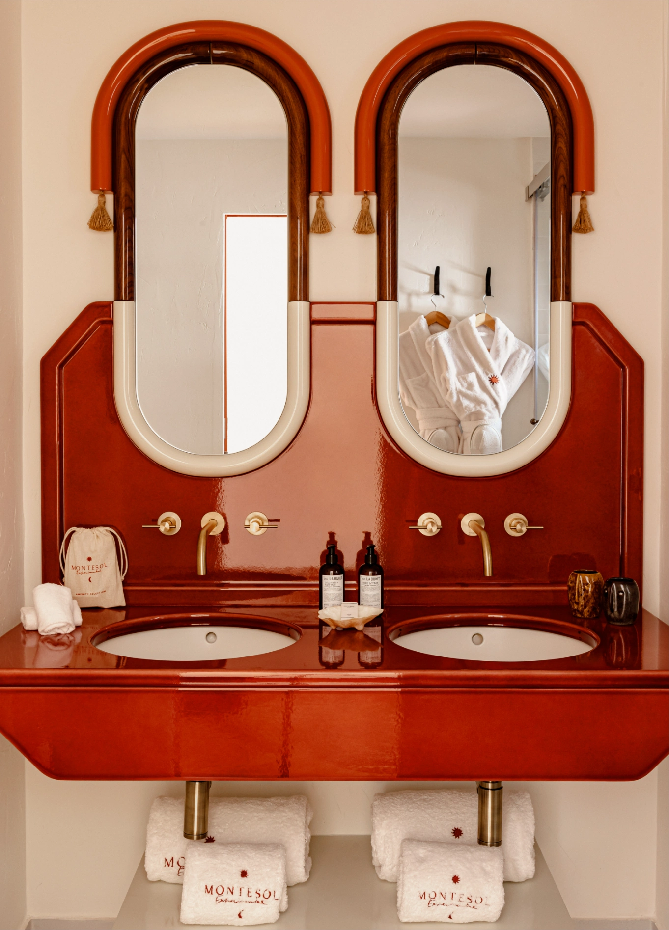 Refined bathroom at Experimental Beach Ibiza with a double integrated sink, oval mirrors, and red decorative accents.