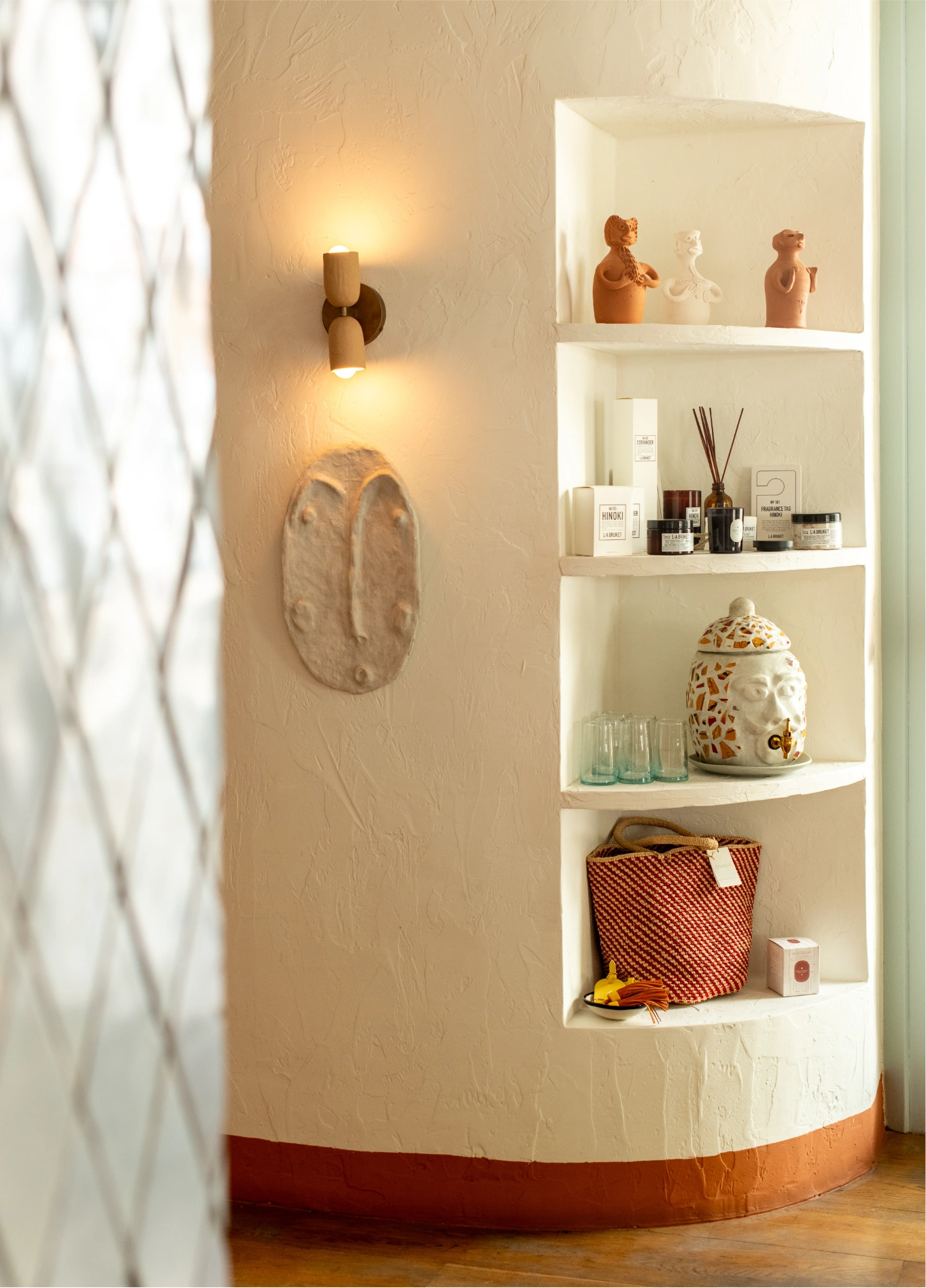A curved, illuminated wall niche in a room at the Montesol Experimental hotel, containing decorative objects, with a wall lamp next to it.