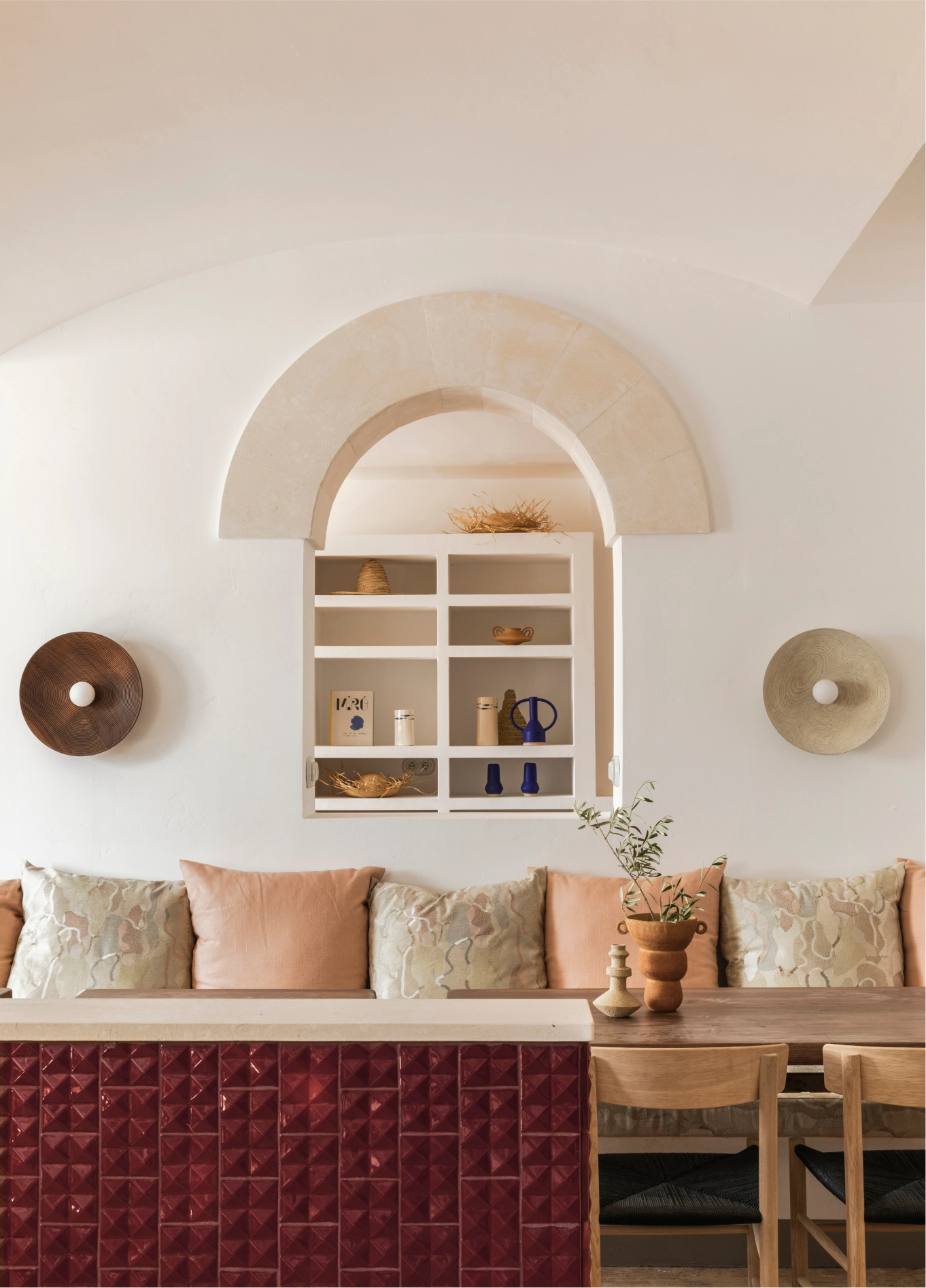 Interior atmosphere of Menorca Experimental with a red tiled counter, shelves built into a wall arch, and a bench decorated with neutral-toned cushions.