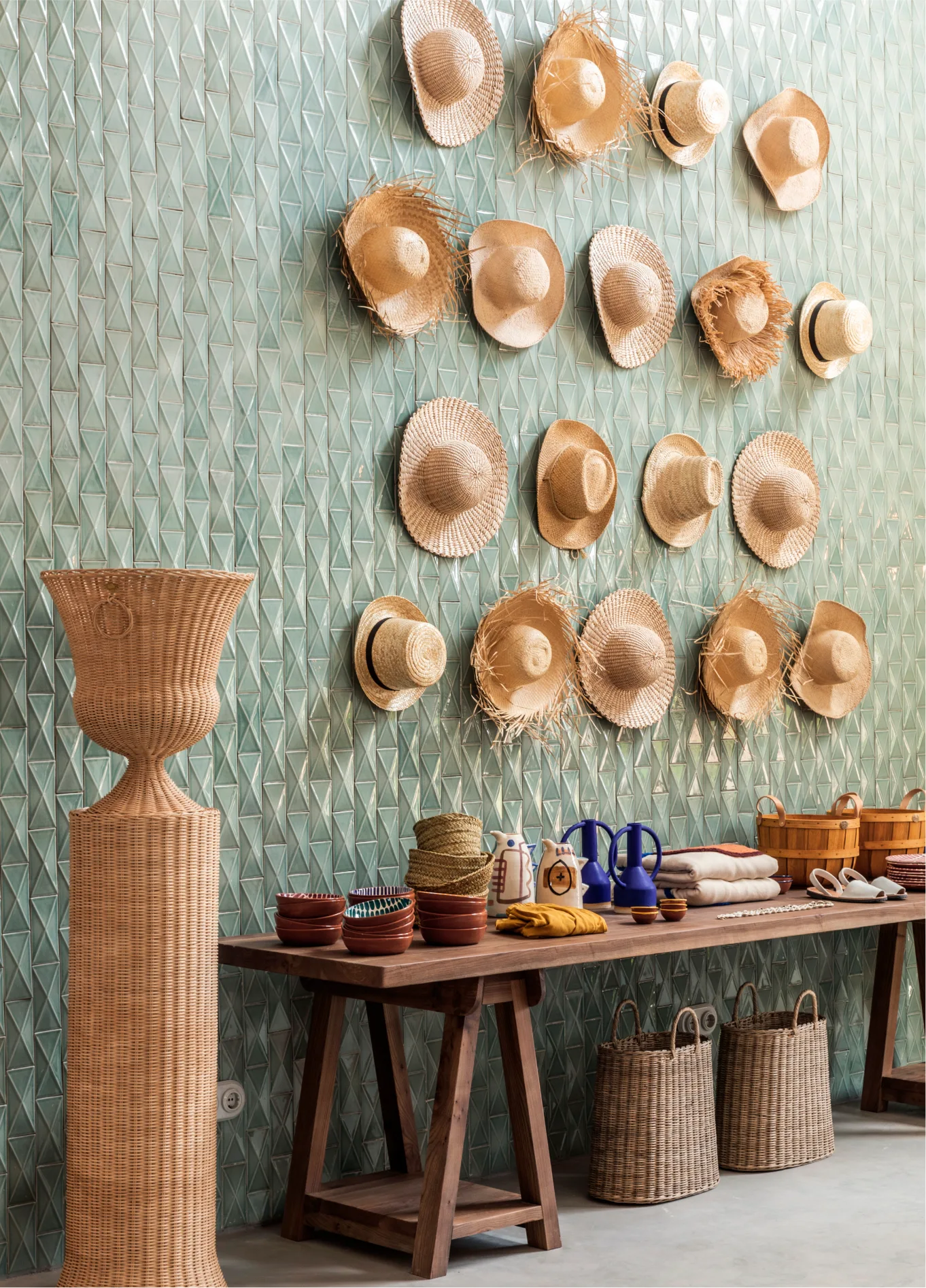 Wall decoration featuring straw hats on a green textured wall, accompanied by a long wooden table with various handcrafted items at Manorca Experimental.