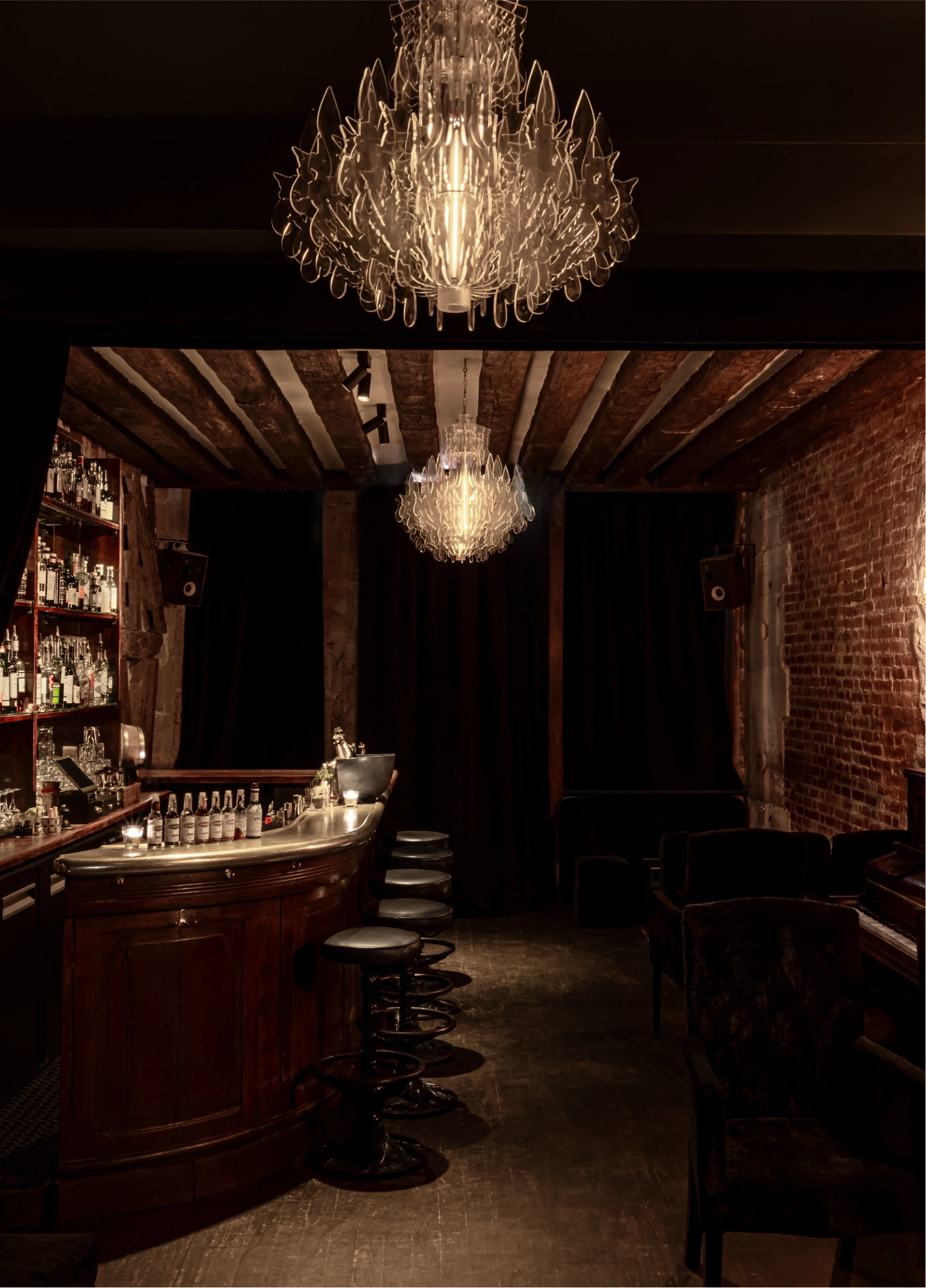 Cozy atmosphere of the Experimental Cocktail Club, showcasing a wooden bar counter, stools, and a decorative chandelier hanging from the ceiling.