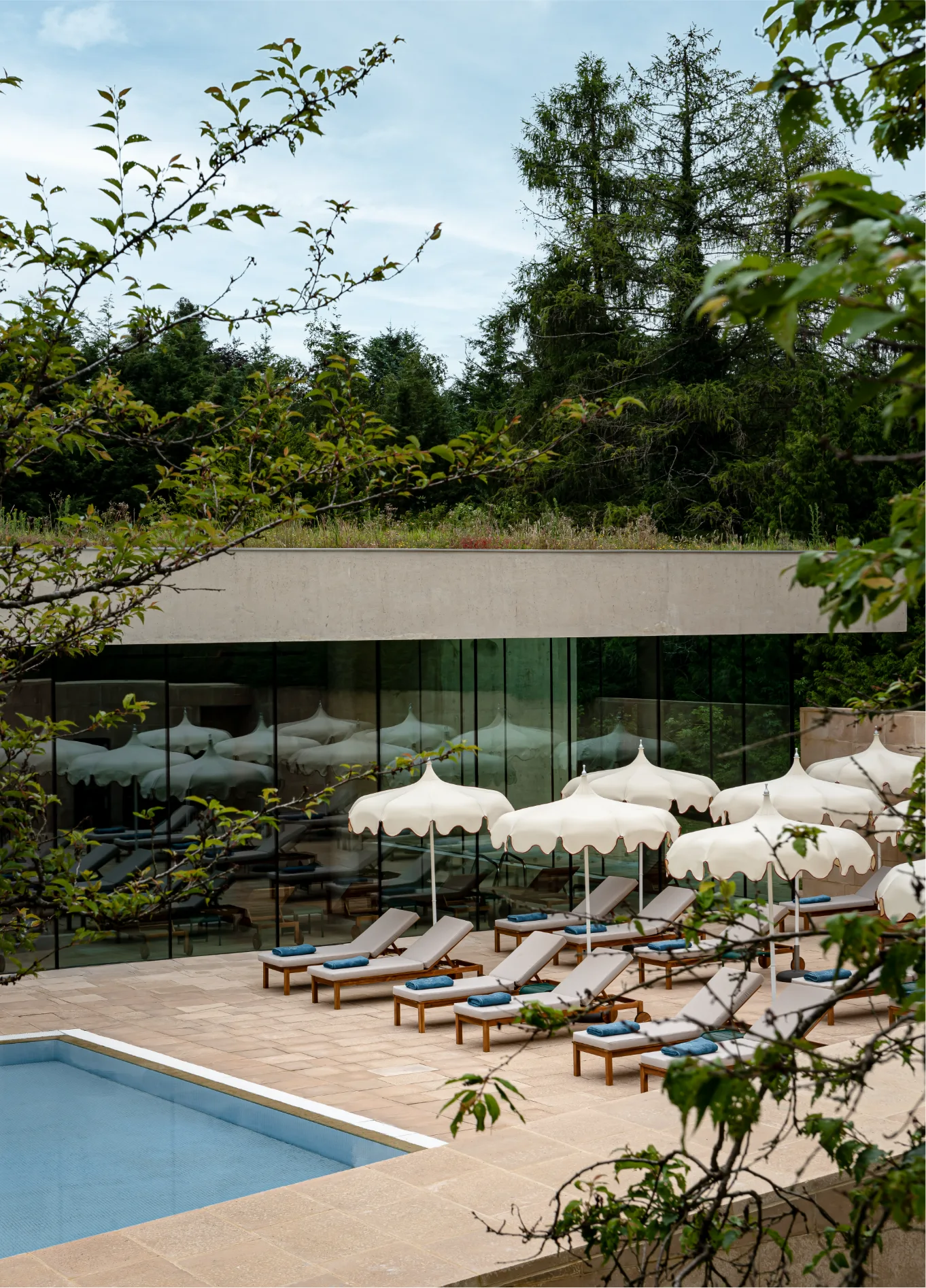 Outdoor swimming pool with sun loungers and parasols at Cowley Manor Spa Hotel, Cotswolds