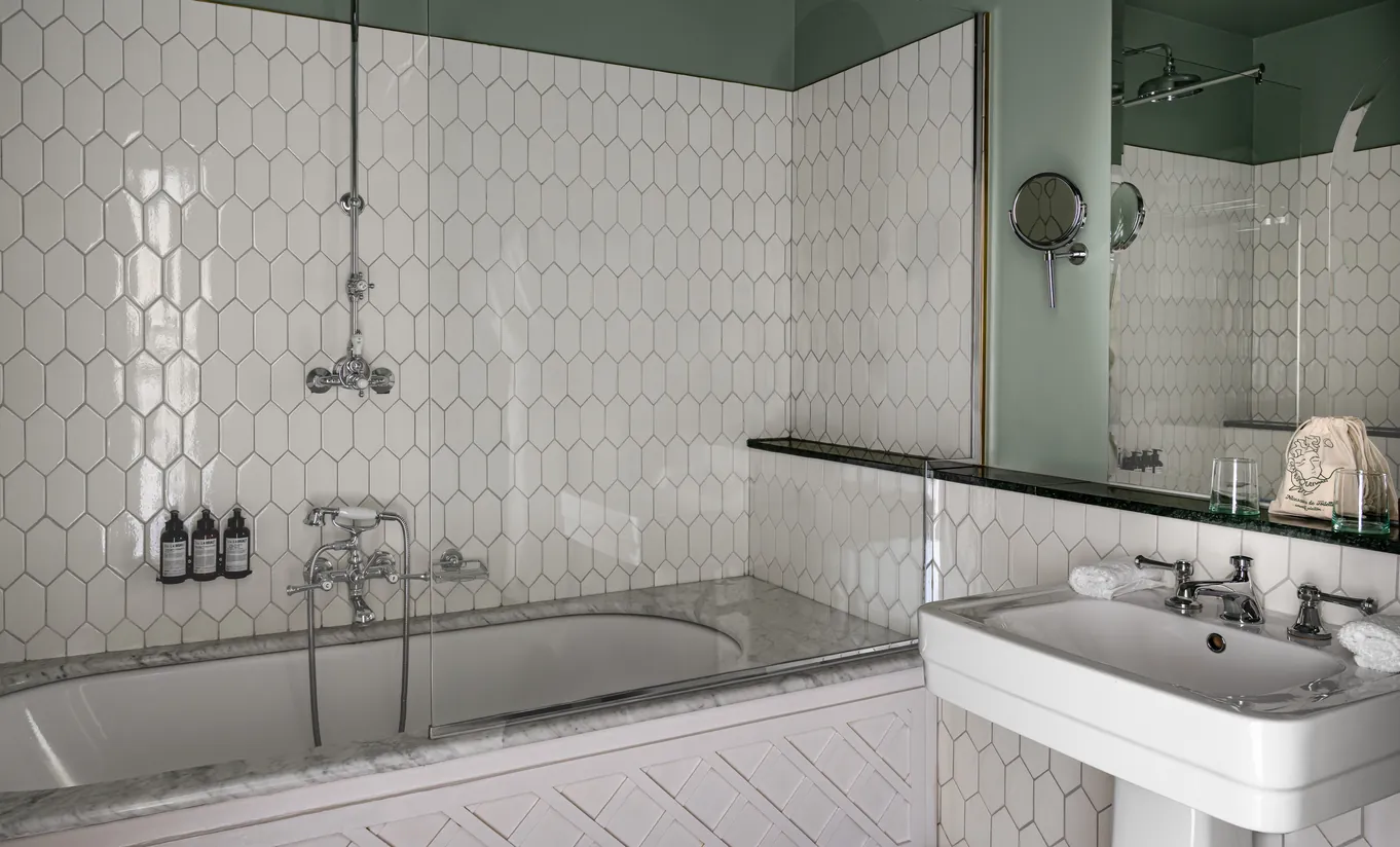 Salle de bain avec baignoire encastrée, carrelage hexagonal blanc et double vasque dans la chambre Uzès de Grands Boulevards Experimental, hôtel boutique sur les Grands Boulevards, Paris