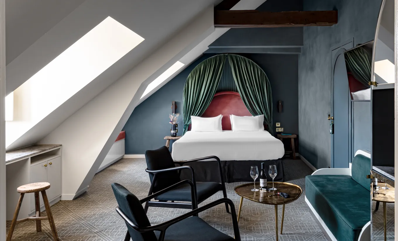 Chambre avec grand lit blanc, tête de lit rouge, drapés vert sauge et fenêtre de toit sous les combles dans la chambre Sous les toits de Grands Boulevards Experimental, hôtel boutique dans le 2e arrondissement de Paris
