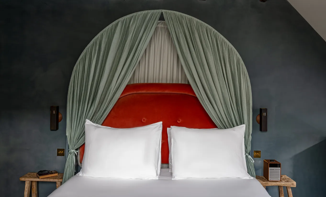 Détail d'un grand lit blanc avec baldaquin drapé vert sauge et tête de lit rouge dans la chambre Sous les toits de Grands Boulevards Experimental, Paris 2e, proche de l'Opéra Garnier