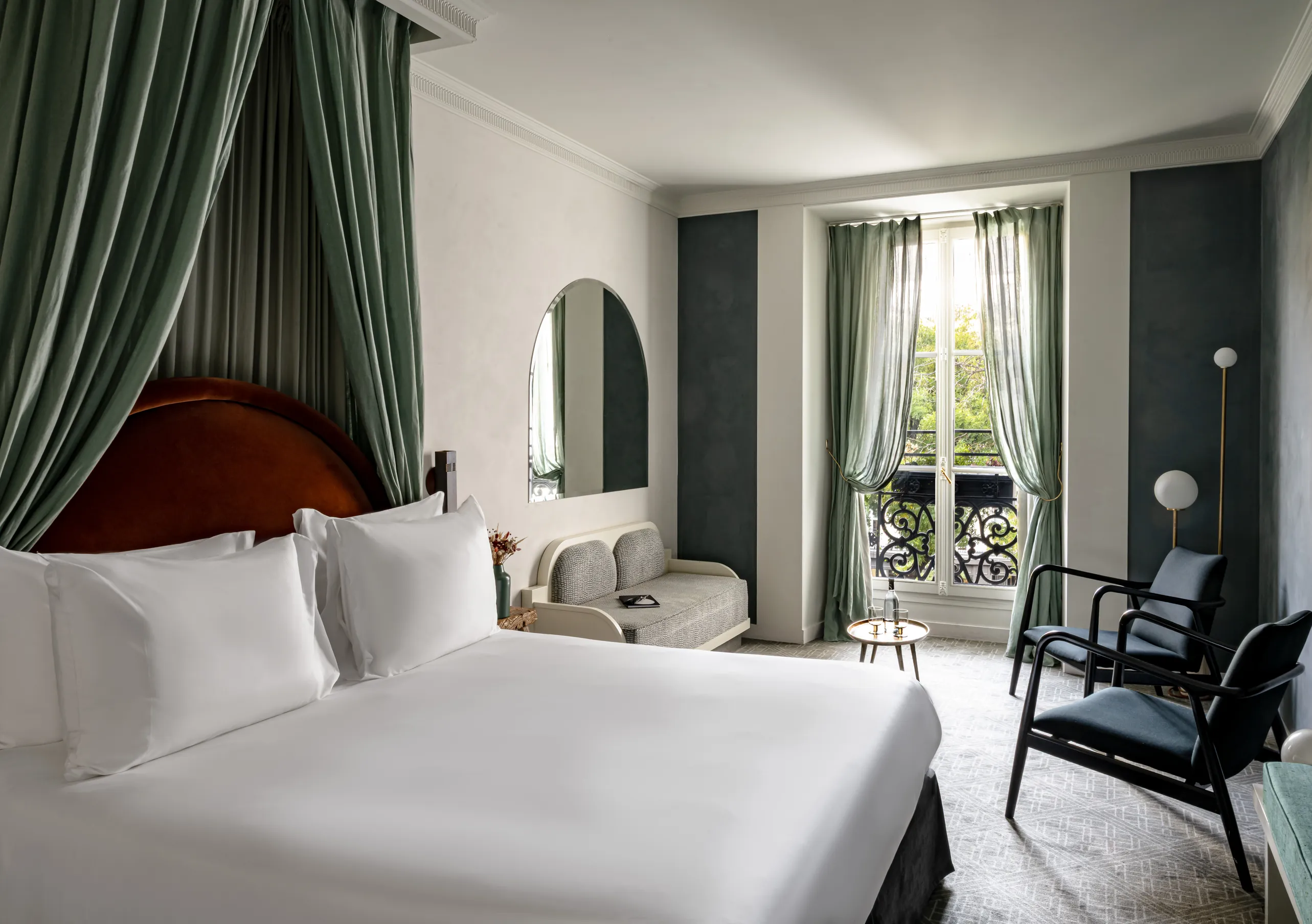 Chambre avec grand lit blanc, rideaux vert sauge, tête de lit rouge et vue sur les toits parisiens dans la chambre Grand Boulevard de Grands Boulevards Experimental, hôtel boutique dans le 2e arrondissement de Paris