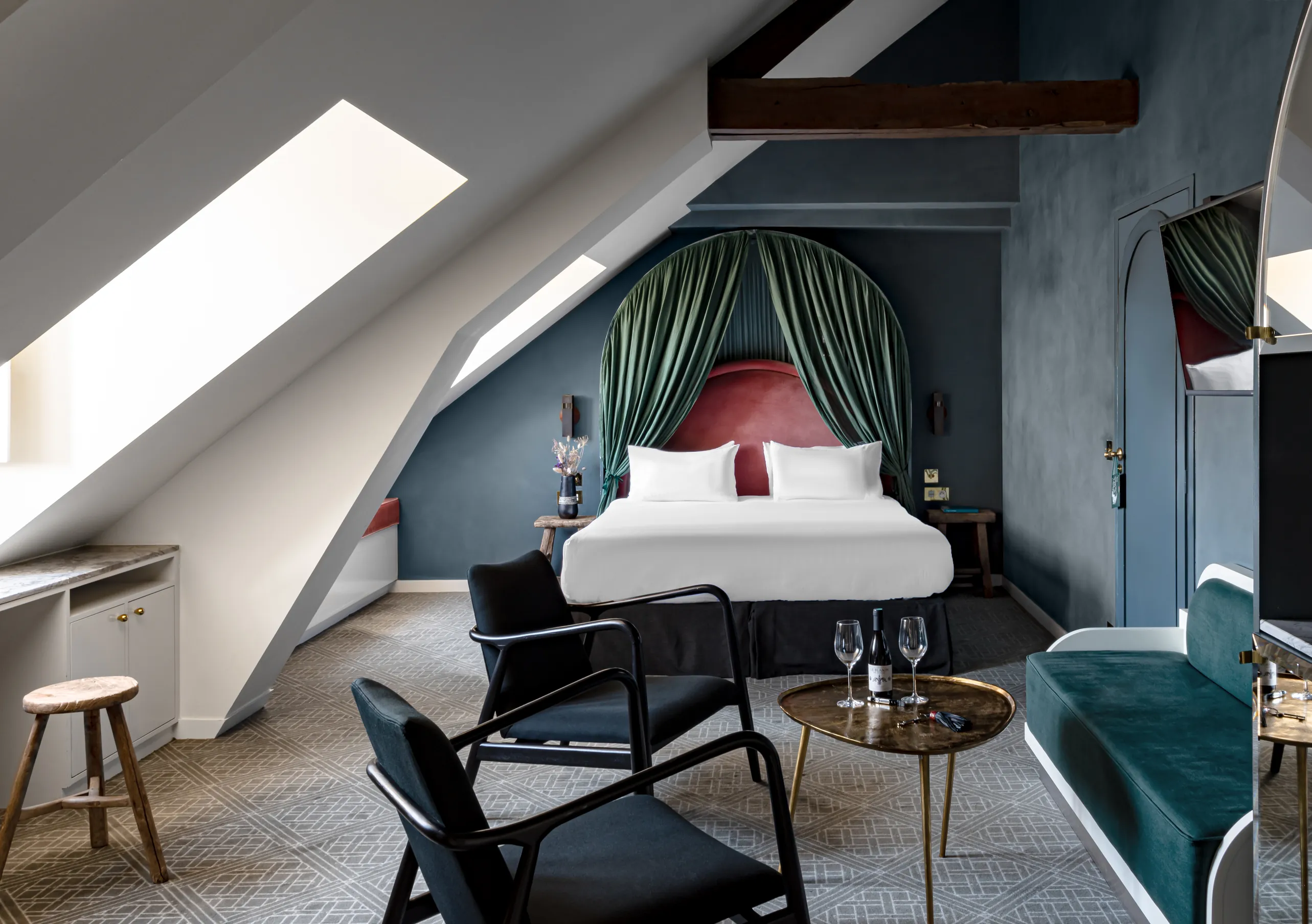 Chambre avec grand lit blanc, tête de lit rouge, drapés vert sauge et fenêtre de toit sous les combles dans la chambre Sous les toits de Grands Boulevards Experimental, hôtel boutique dans le 2e arrondissement de Paris
