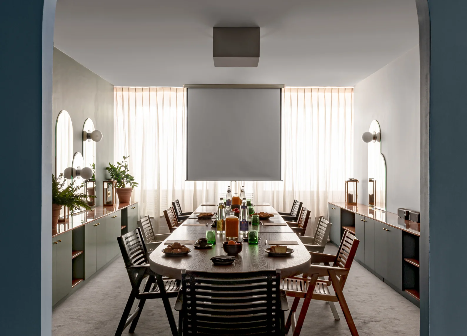 Sala de reuniones privada y luminosa con mesa ovalada de madera, sillas de diferentes estilos y pantalla de proyección en el hotel boutique experimental Grands Boulevards, en el distrito 2 de París