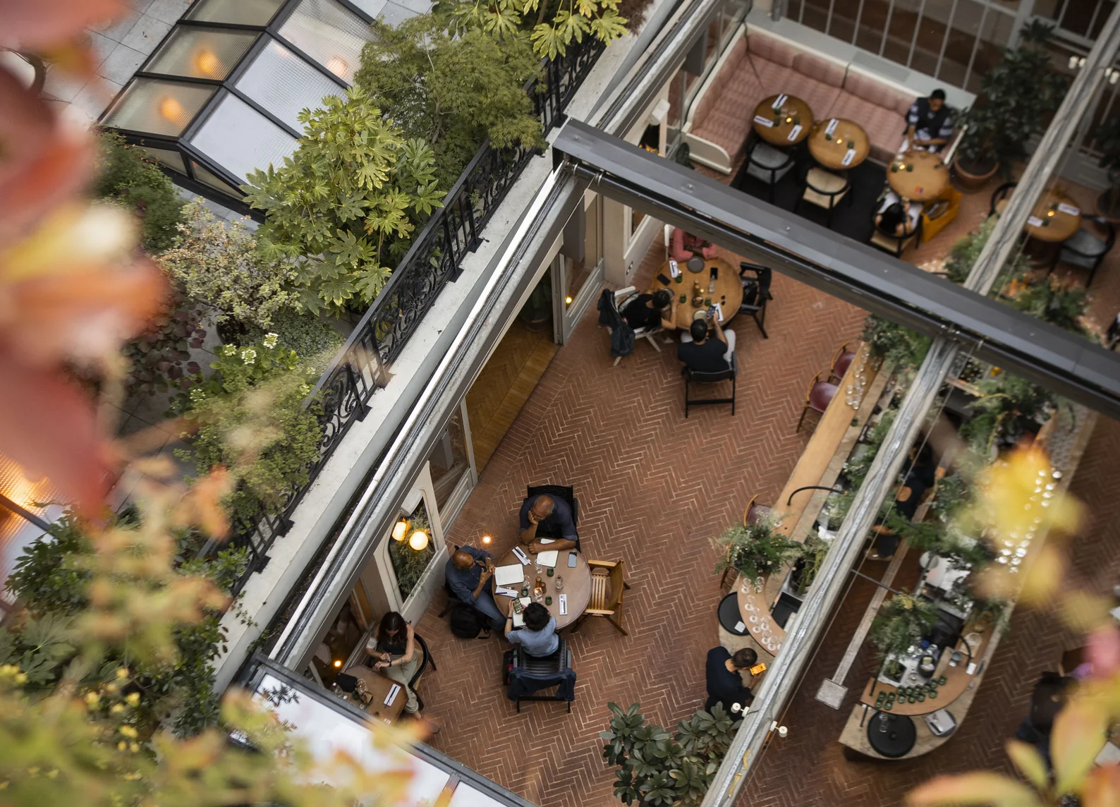 Vista aérea de la terraza de ladrillo en espiga, rodeada de exuberante vegetación, con comensales disfrutando de la cena en Grands Boulevards Experimental, un restaurante de alta cocina situado en el centro de París