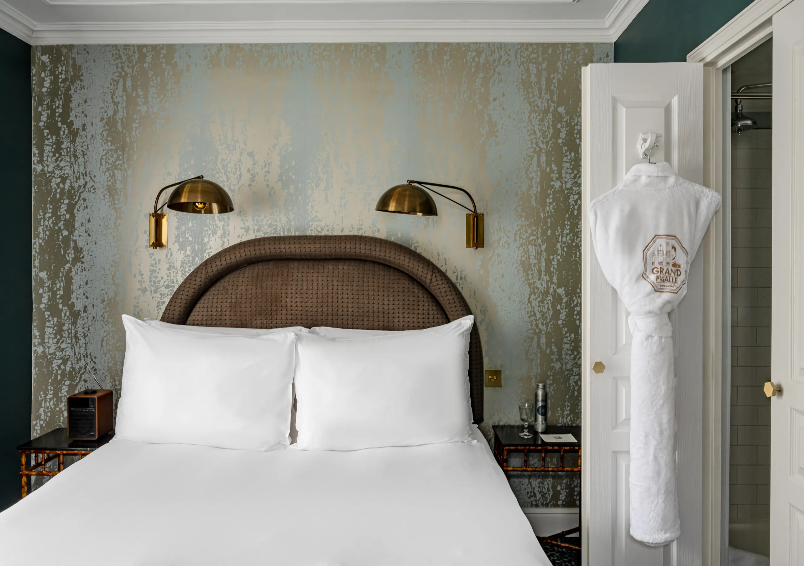 Chambre avec grand lit blanc, tête de lit tressée et murs bleu canard avec papier peint texturé doré dans la chambre Sopi de Grand Pigalle Experimental, hôtel boutique dans le 9e arrondissement de Paris, Pigalle