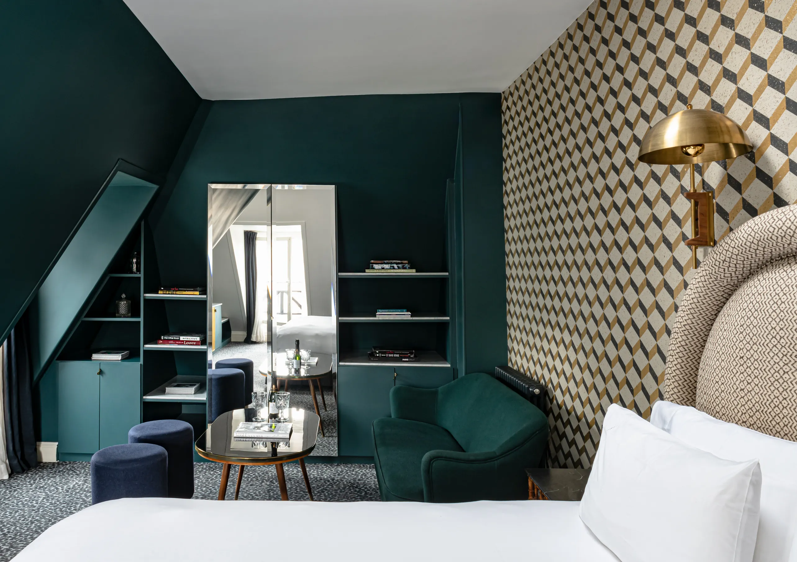 Chambre avec grand lit blanc, tête de lit à motifs géométriques, murs bleu canard et miroir doré dans la Suite Junior Sous les Toits de Grand Pigalle Experimental, hôtel boutique dans le 9e arrondissement de Paris, Pigalle