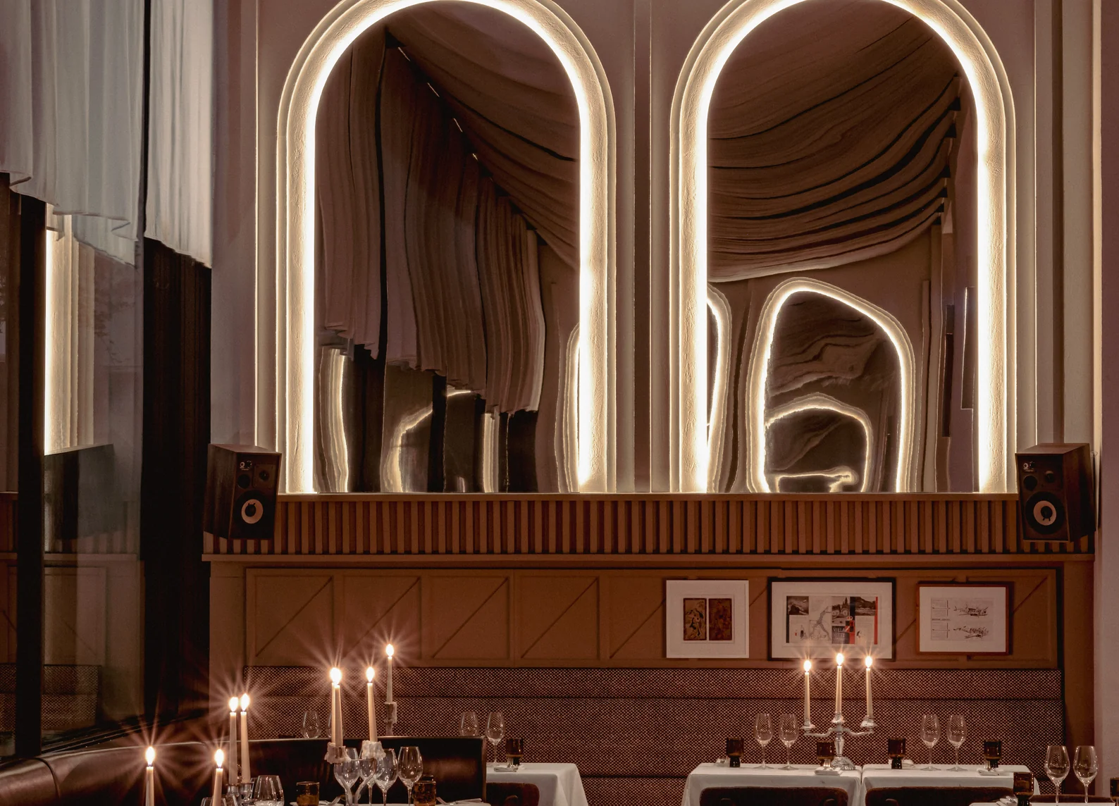 Dos espejos arqueados retroiluminados sobre paneles de madera estriada y mesas con manteles blancos iluminadas por velas en el restaurante Temple & Chapon, del Hotel Experimental Marais, en París