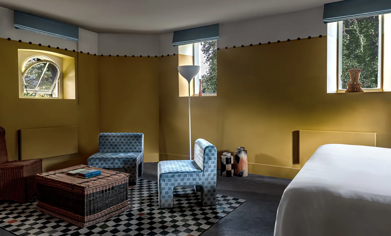 Coin salon avec méridienne, sol à damier et murs jaune moutarde dans la chambre Wildflower de Cowley Manor Experimental, retraite à la campagne dans les Cotswolds
