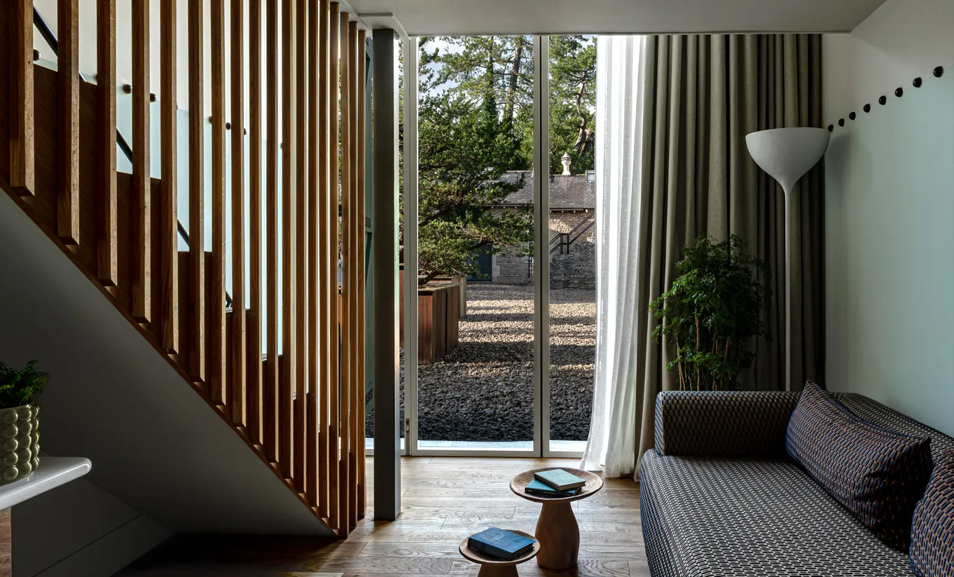 Salon lumineux avec cloisons en bois lamellé, canapé et grandes fenêtres donnant sur le domaine dans la chambre Treehouse de Cowley Manor Experimental, Cotswolds