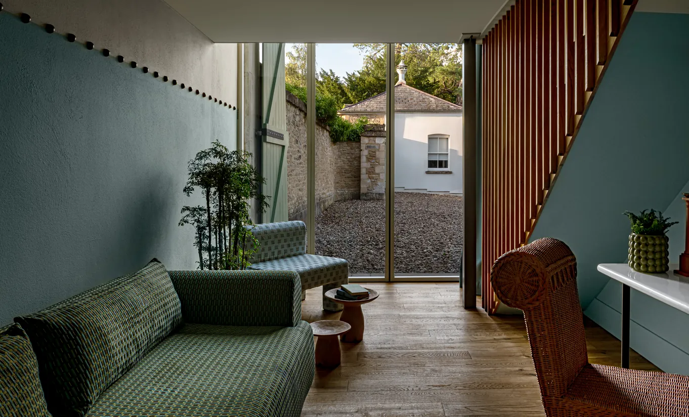 Salon avec canapé vert, rideaux bordeaux et cour intérieure ouverte avec plantes dans la Chambre Alpaga de Cowley Manor Experimental, hôtel de luxe dans les Cotswolds