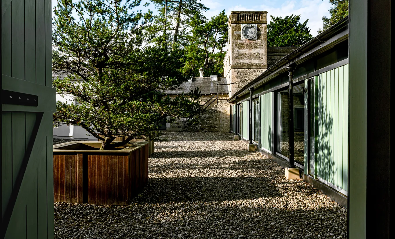 Allée extérieure avec bonsaï et chemin en galets menant à la chambre Treehouse de Cowley Manor Experimental, retraite unique à la campagne dans les Cotswolds