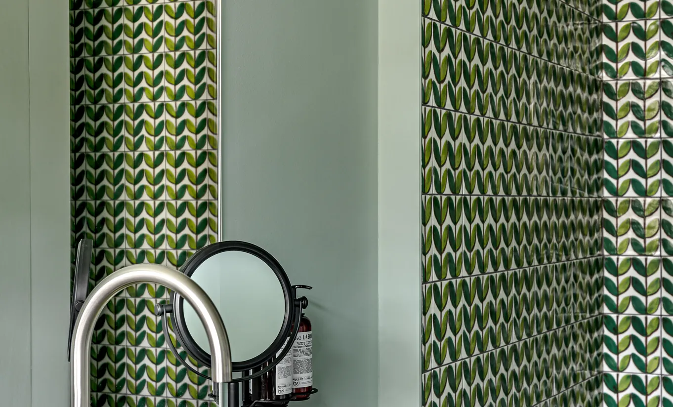 Salle de bain avec carrelage en chevrons vert, miroir rond et robinetterie dorée dans la chambre Petite Cowley de Cowley Manor Experimental, hôtel de luxe dans les Cotswolds