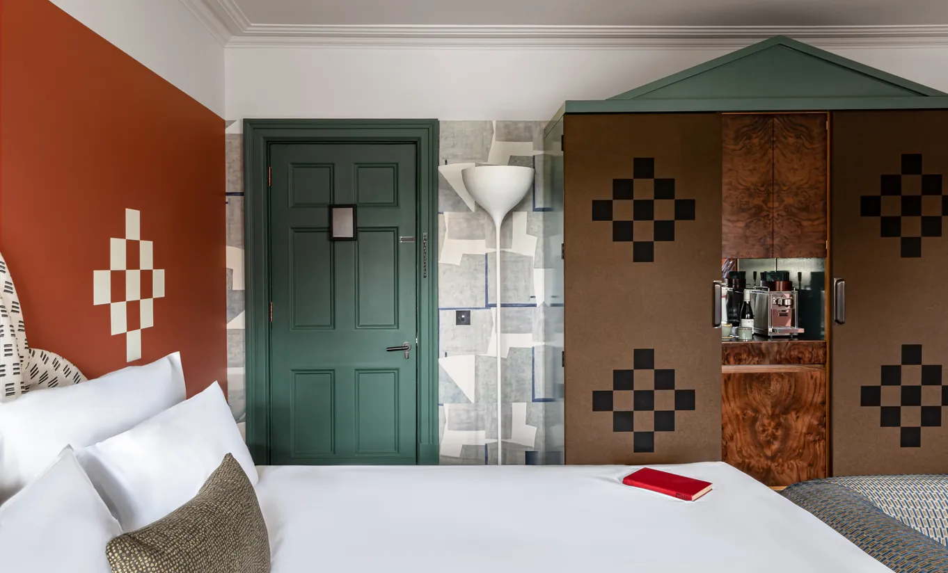 Chambre avec grand lit blanc, murs terracotta, porte vert foncé et armoire à motifs damier dans la chambre Petite Cowley de Cowley Manor Experimental, Cotswolds