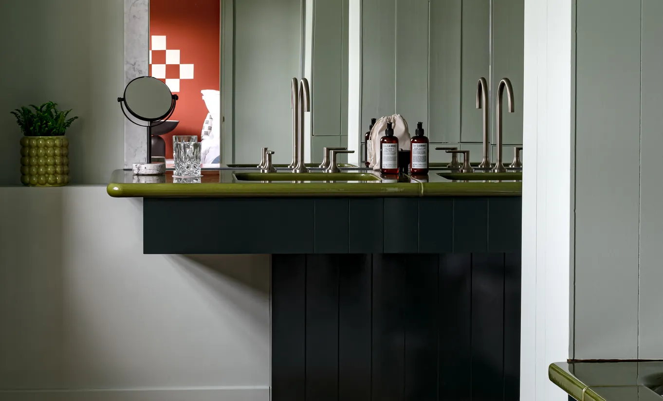Détail d'une cheminée avec manteau vert foncé et produits de soin disposés sur l'étagère dans la chambre Petite Cowley de Cowley Manor Experimental, Cotswolds
