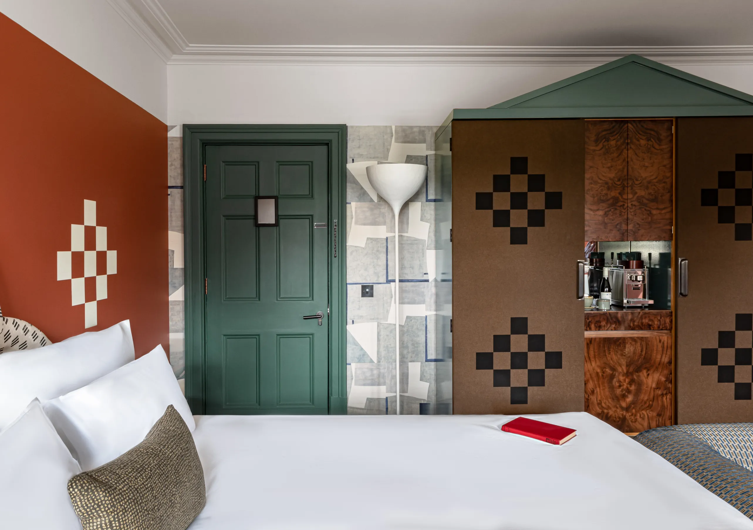 Chambre avec grand lit blanc, murs terracotta, porte vert foncé et armoire à motifs damier dans la chambre Petite Cowley de Cowley Manor Experimental, Cotswolds