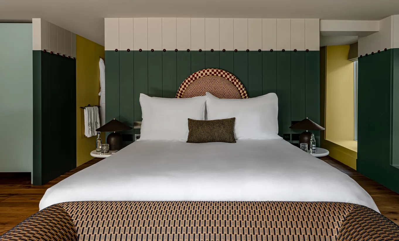 Chambre avec lit king-size, murs jaune moutarde, boiseries vert foncé et tête de lit en rotin dans la chambre Wildflower avec terrasse de Cowley Manor Experimental, Cotswolds