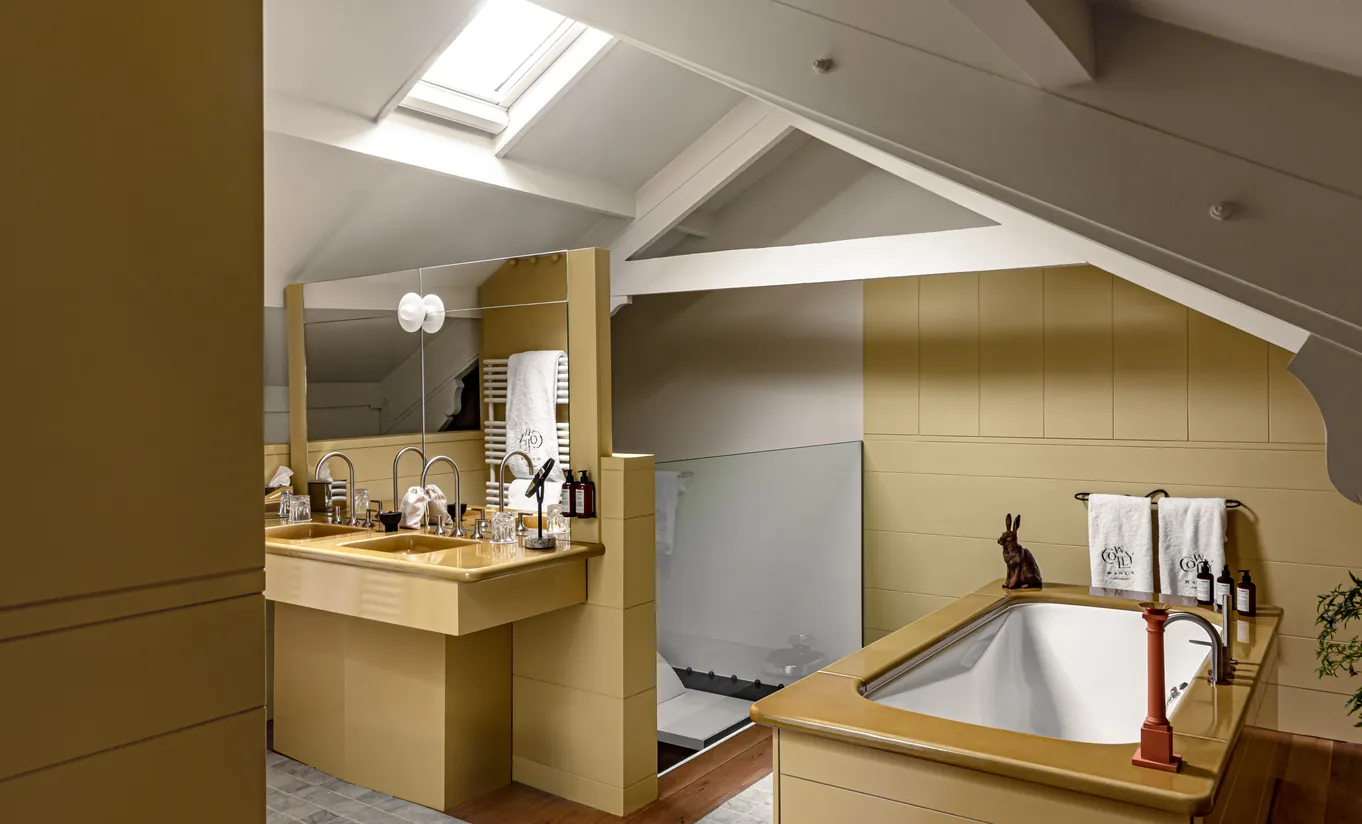 Salle de bain avec baignoire encastrée, carrelage jaune moutarde et fenêtre de toit dans la chambre Wildflower avec terrasse de Cowley Manor Experimental, hôtel spa de luxe dans les Cotswolds