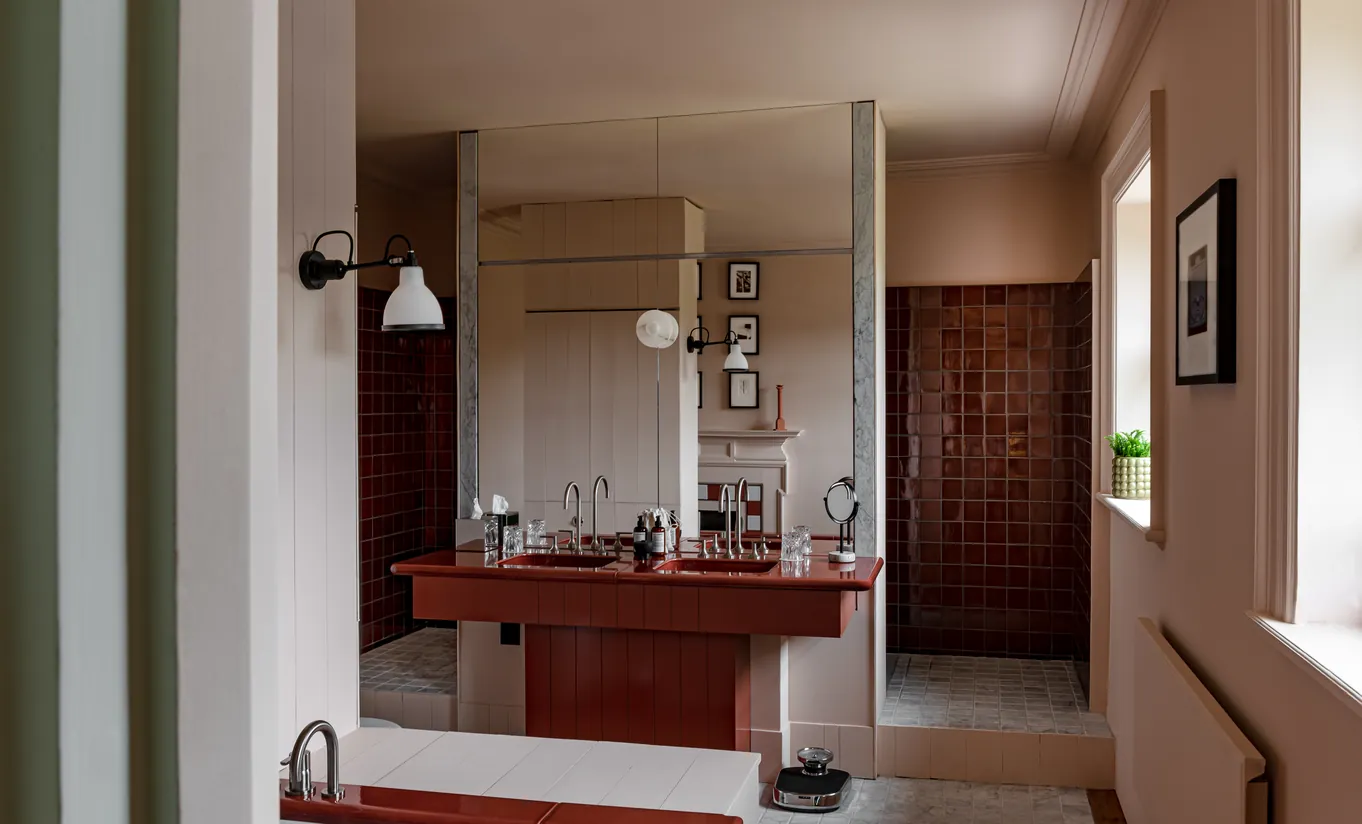 Salle de bain avec double vasque en marbre rouge, murs en bois sombre et éclairage chaleureux dans la chambre Water Lily de Cowley Manor Experimental, hôtel spa de luxe dans les Cotswolds
