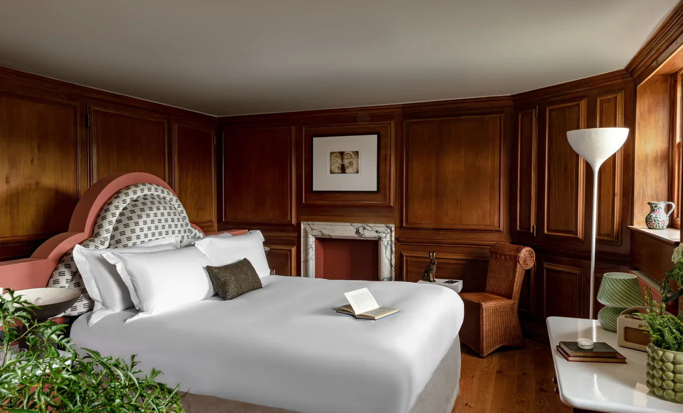 Chambre avec grand lit blanc, boiseries sombres, cheminée et plantes d'intérieur dans la chambre Water Lily de Cowley Manor Experimental, Cotswolds