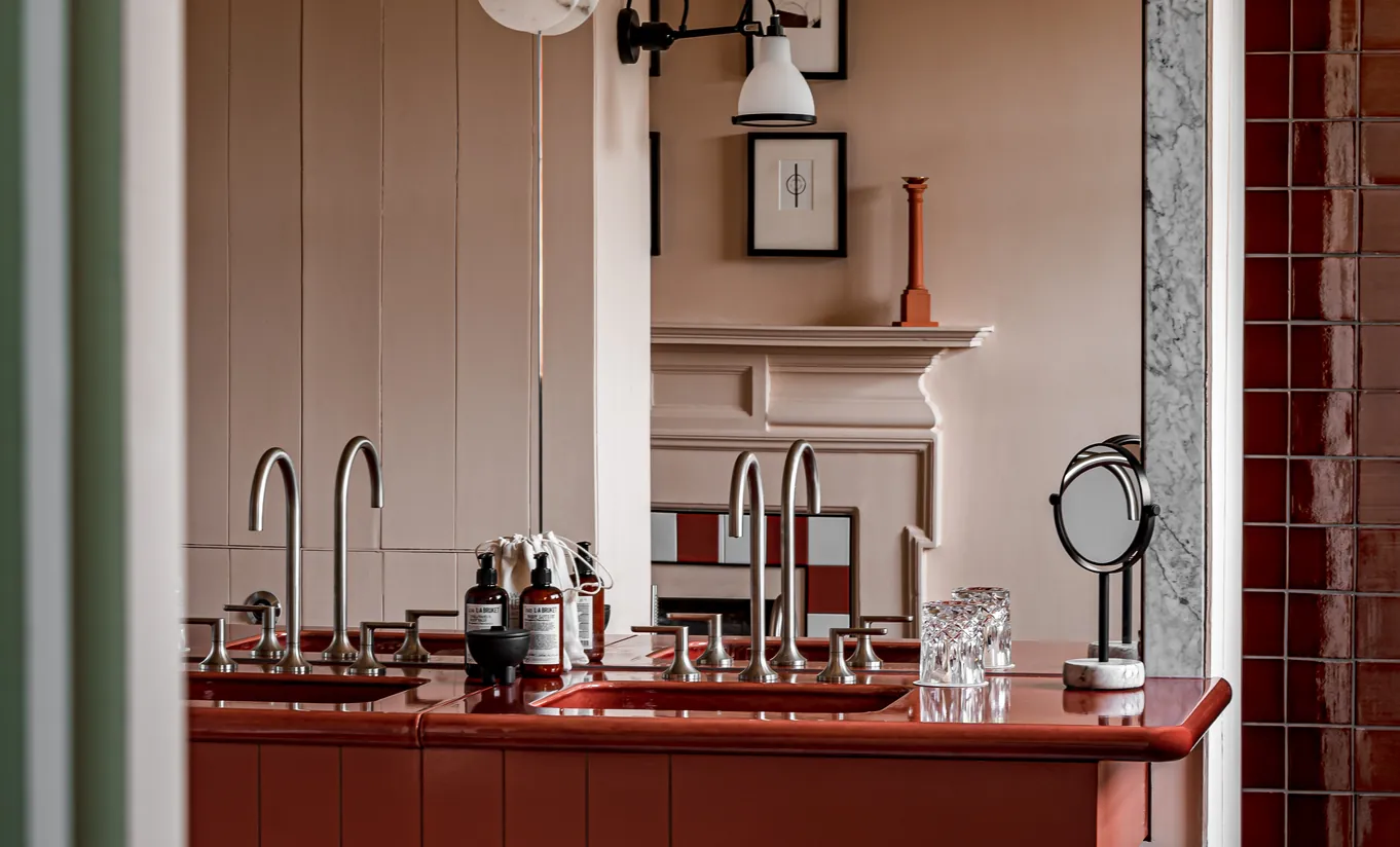 Détail d'un espace coiffeuse avec plan de travail en marbre rouge, boiseries sombres et éclairage vintage dans la chambre Water Lily de Cowley Manor Experimental, hôtel de luxe dans les Cotswolds