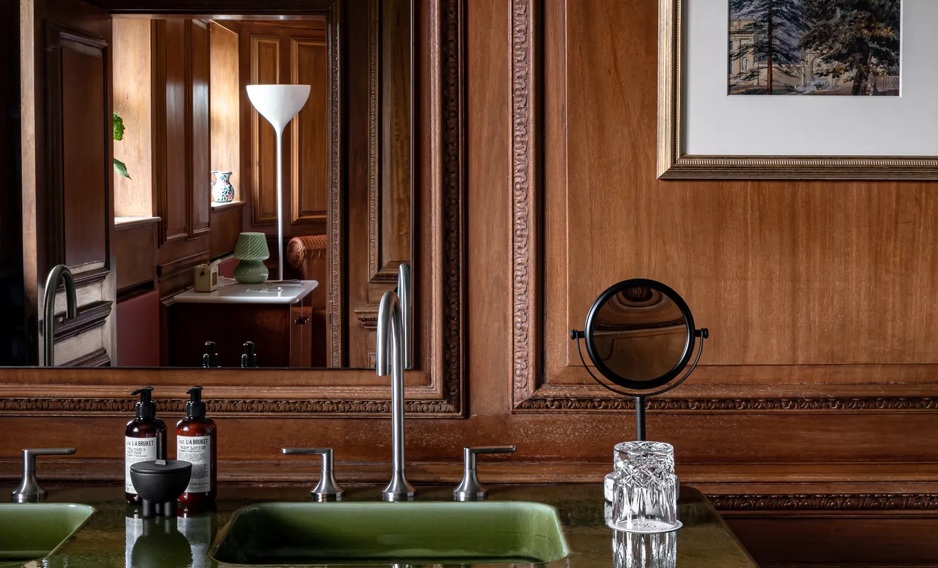 Salle de bain avec boiseries sombres, double vasque verte et miroir de courtoisie vintage dans la chambre Water Lily de Cowley Manor Experimental, Cotswolds