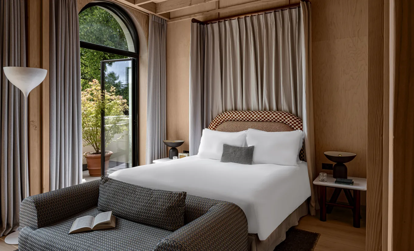 Chambre avec grand lit blanc, tête de lit tressée et fenêtres en arche avec rideaux en lin dans la chambre Waterlily with Terrace de Cowley Manor Experimental, Cotswolds