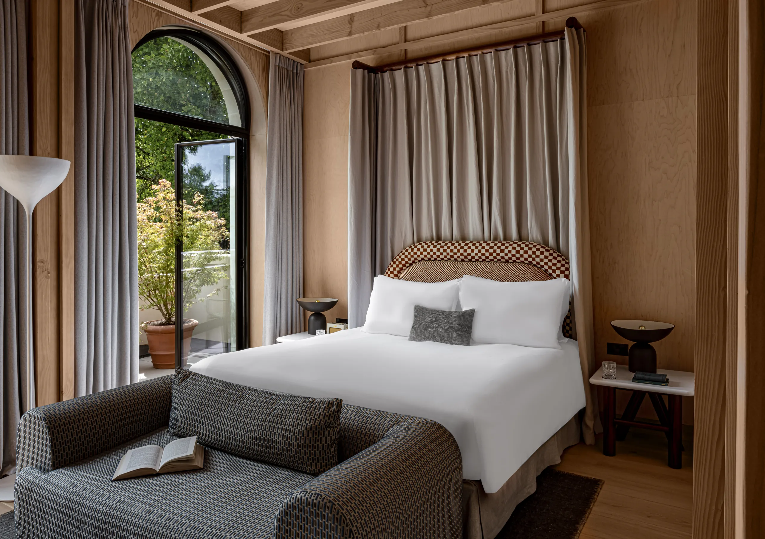 Chambre avec grand lit blanc, tête de lit tressée et fenêtres en arche avec rideaux en lin dans la chambre Waterlily with Terrace de Cowley Manor Experimental, Cotswolds