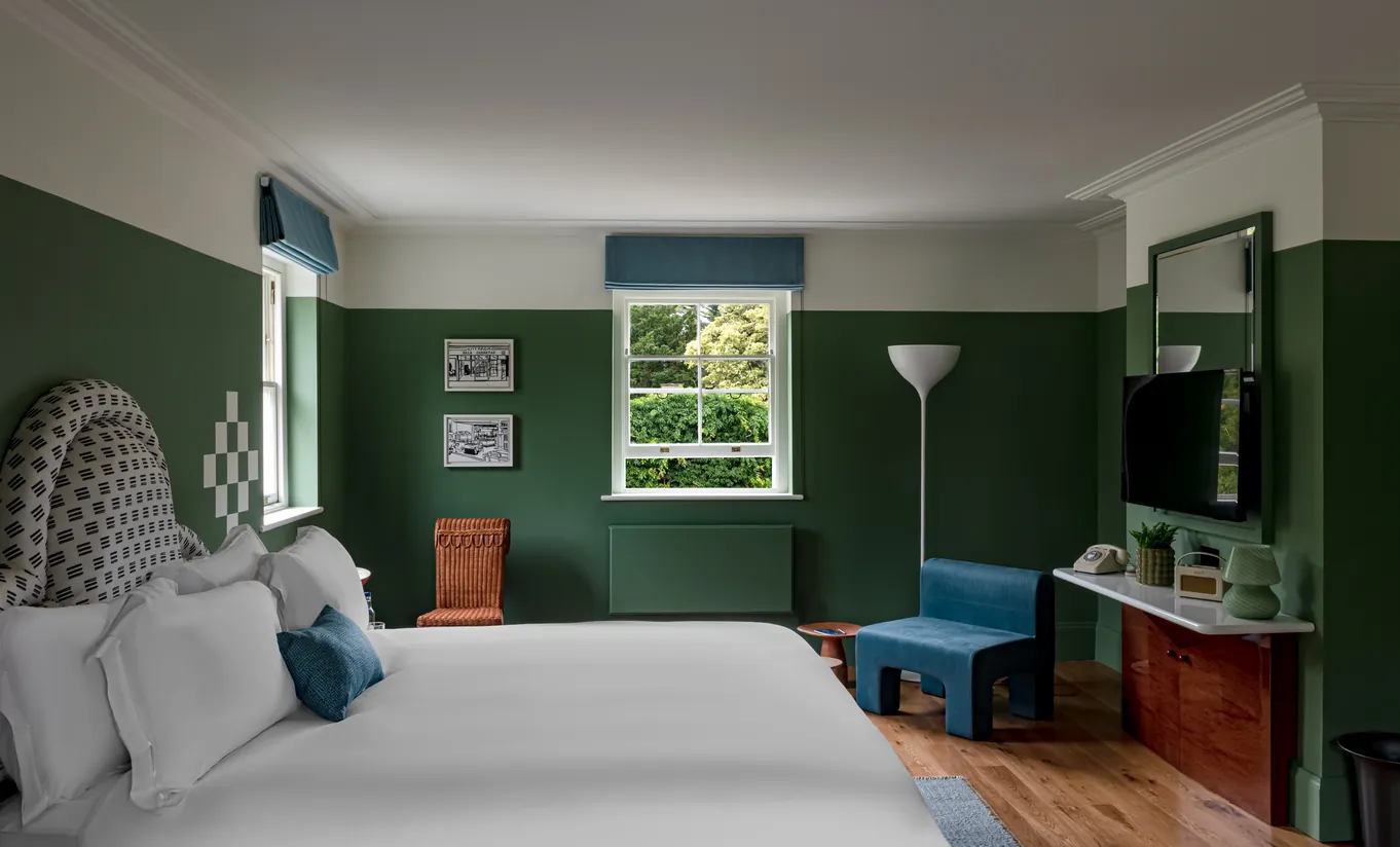 Chambre avec grand lit blanc, murs vert foncé et banc bleu en pied de lit dans la Churns River Junior Suite de Cowley Manor Experimental, Cotswolds