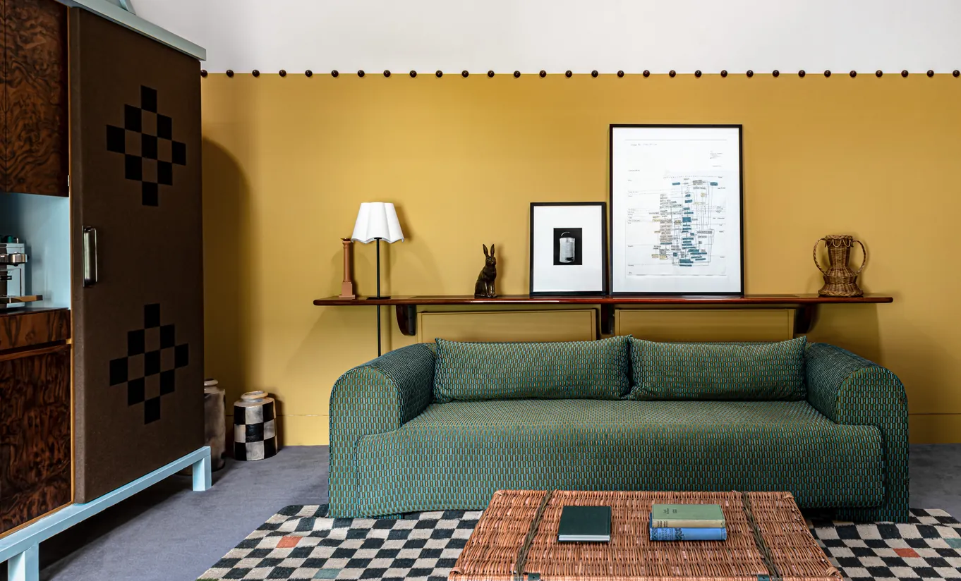 Salon de la Churns River Junior Suite avec un canapé vert, des murs jaune moutarde et un tapis à motifs géométriques à Cowley Manor Experimental, hôtel de luxe dans les Cotswolds.