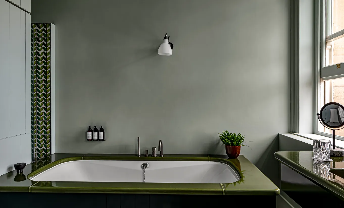 Salle de bain avec baignoire encastrée verte, murs vert sauge et éclairage chaleureux dans la Swan Lake Suite de Cowley Manor Experimental, hôtel spa de luxe dans les Cotswolds