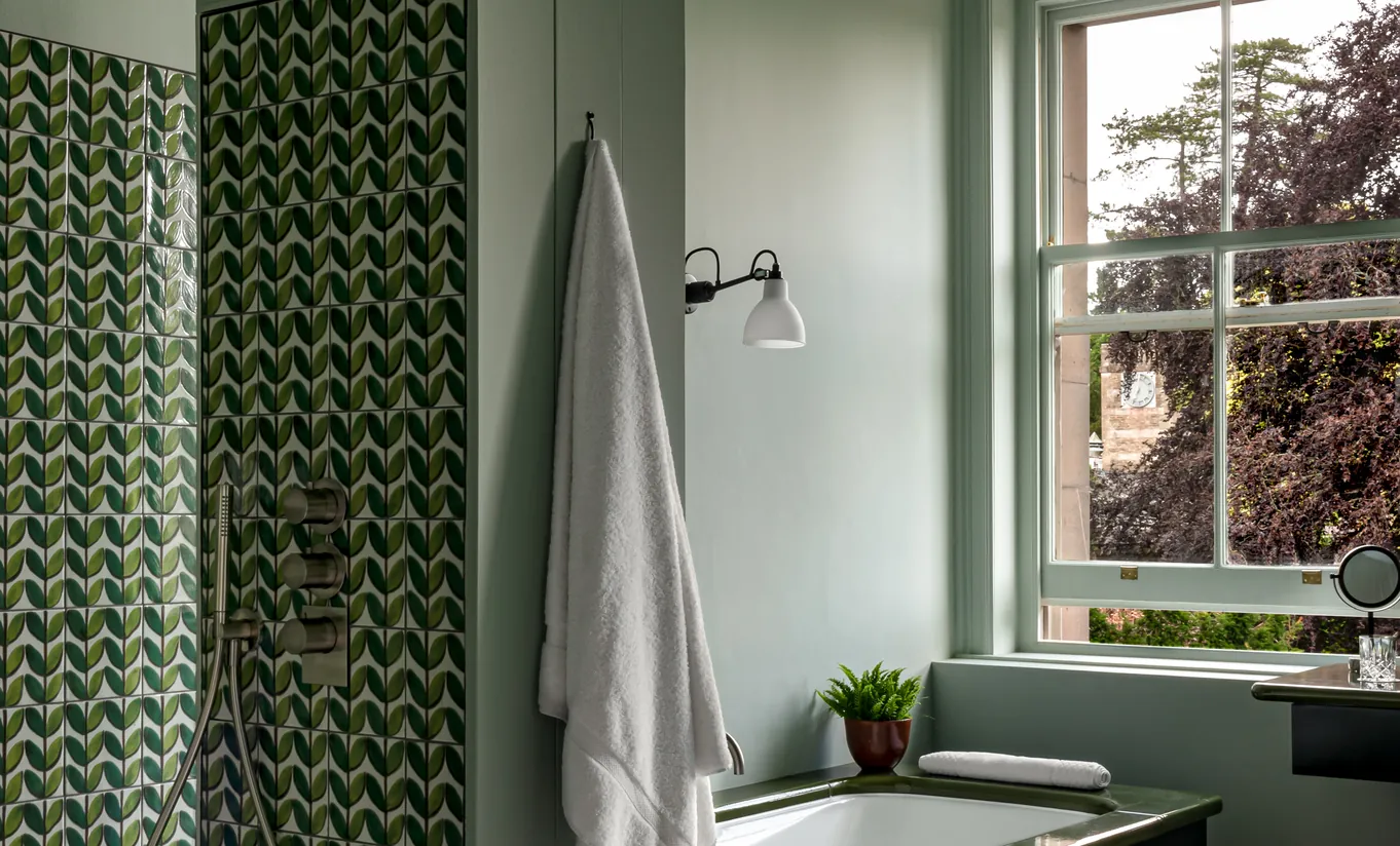 Salle de bain de la Swan Lake Suite avec carrelage vert en chevrons, douche à l'italienne et vue sur le jardin à Cowley Manor Experimental, dans les Cotswolds.