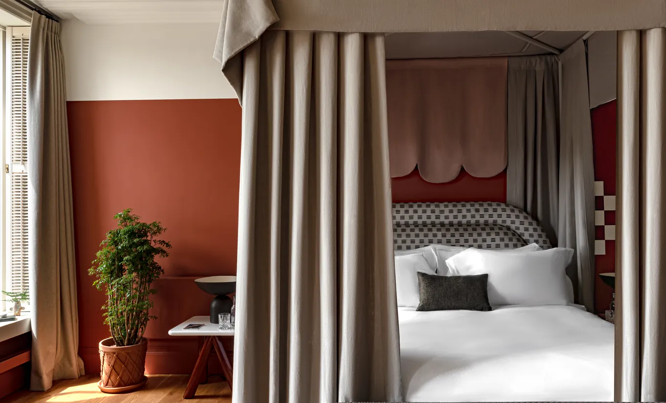 Chambre avec lit à baldaquin, murs terracotta et rideaux en lin au sol dans la Swan Lake Suite de Cowley Manor Experimental, retraite de luxe à la campagne dans les Cotswolds