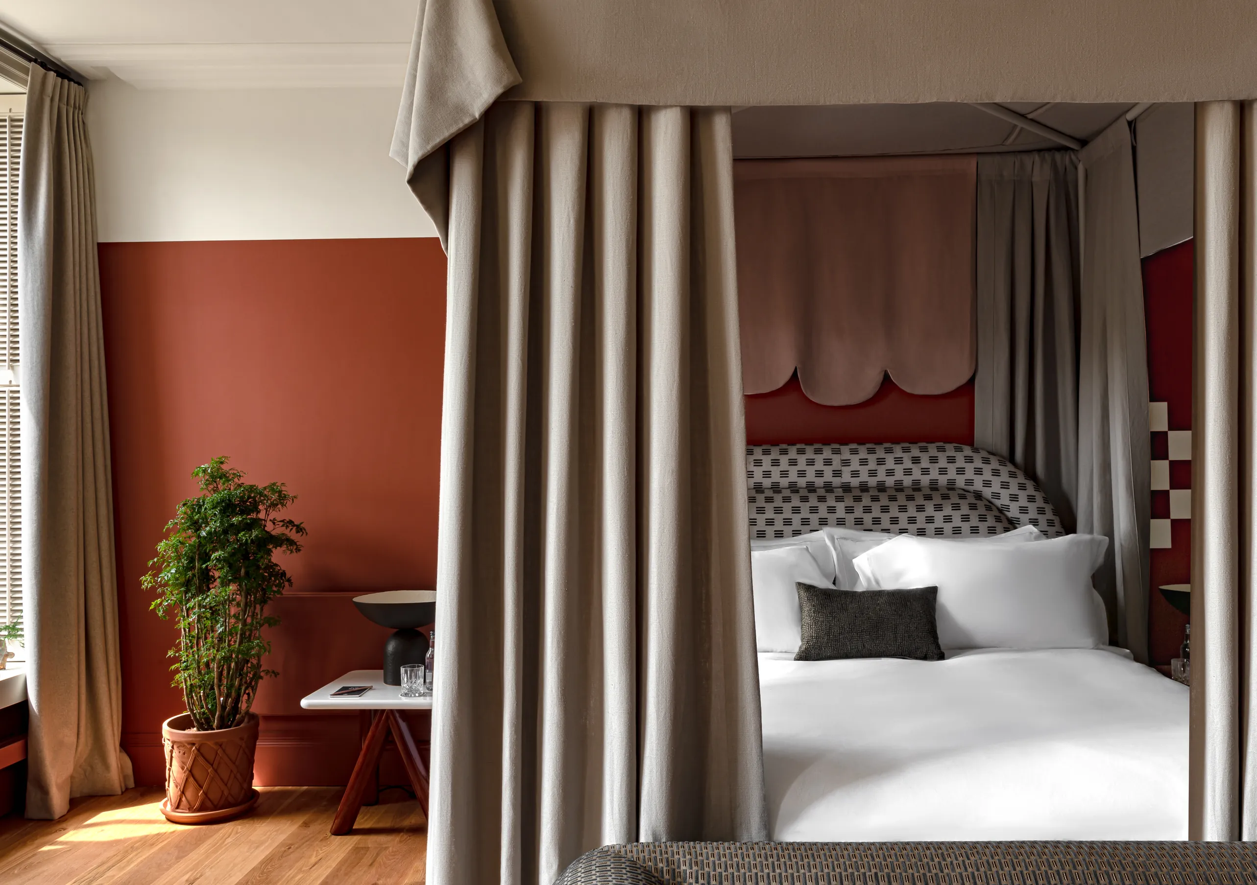 Chambre avec lit à baldaquin, murs terracotta et rideaux en lin au sol dans la Swan Lake Suite de Cowley Manor Experimental, retraite de luxe à la campagne dans les Cotswolds
