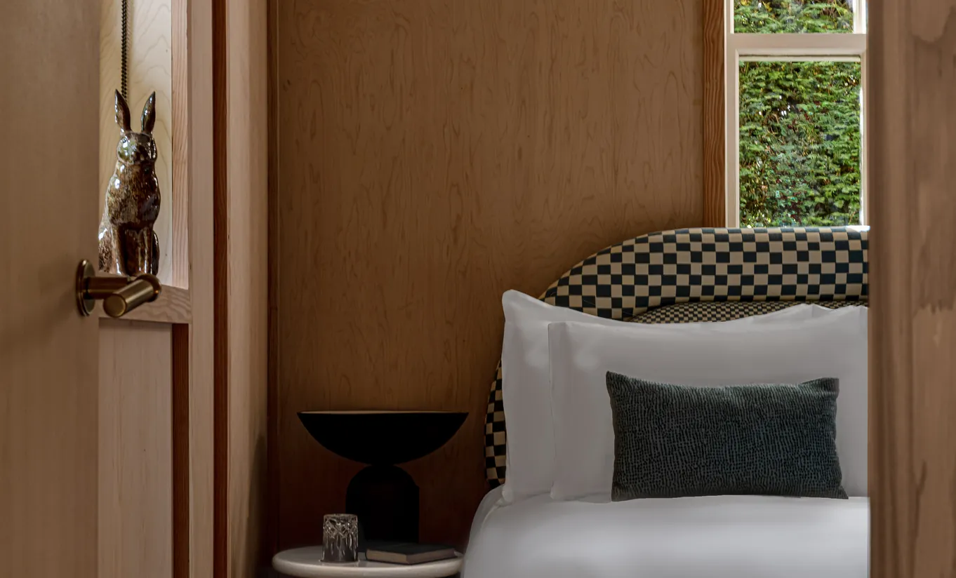 Détail de lit avec linge blanc, coussins à motifs et sculpture en bois dans la Grand Cowley Manor Suite de Cowley Manor Experimental, Cotswolds