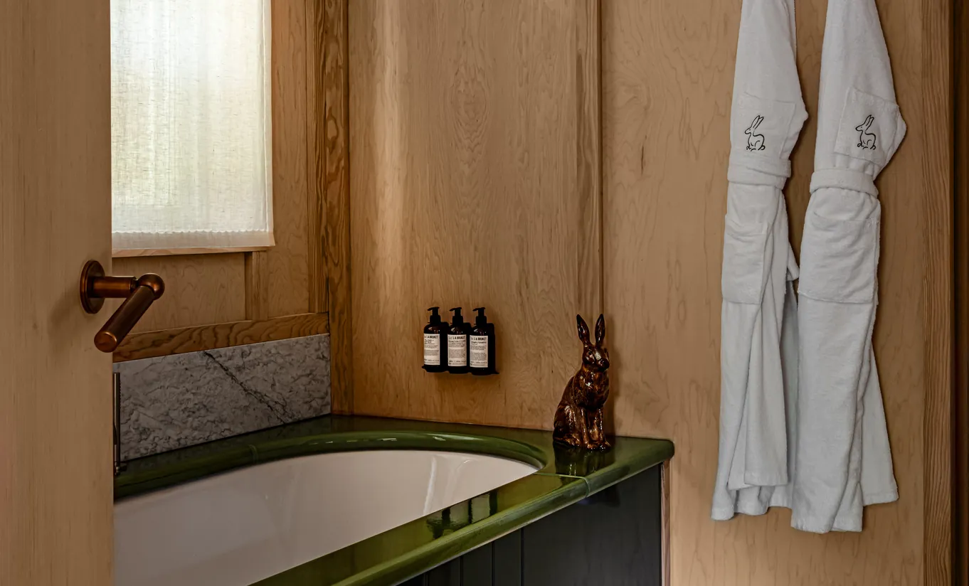 Salle de bain avec baignoire îlot verte, boiseries et peignoirs blancs dans la Grand Cowley Manor Suite de Cowley Manor Experimental, retraite de luxe dans les Cotswolds