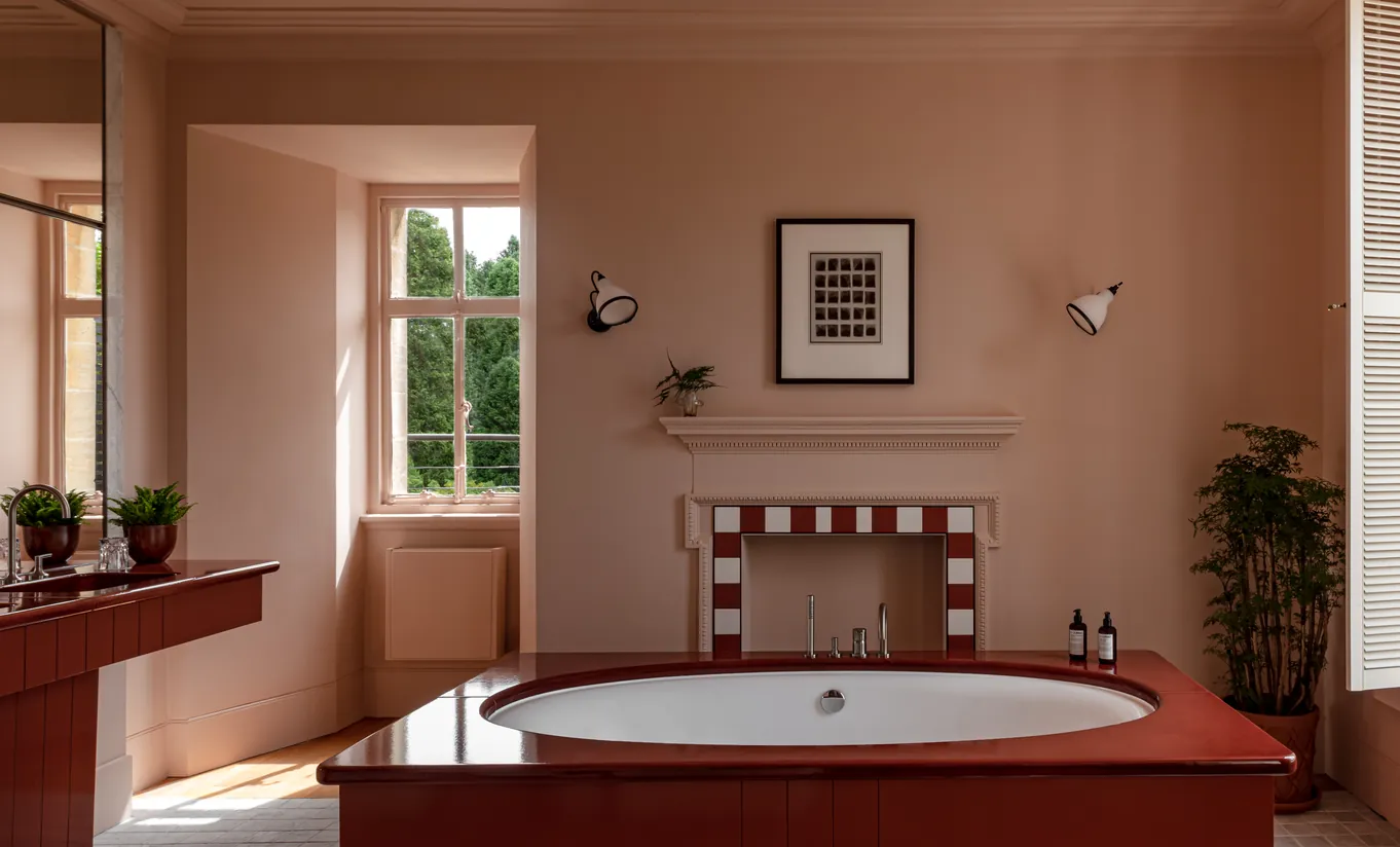 Salle de bain avec baignoire ovale, murs terracotta et cheminée en carrelage rouge et blanc dans la Cowley Manor Suite de Cowley Manor Experimental, Cotswolds